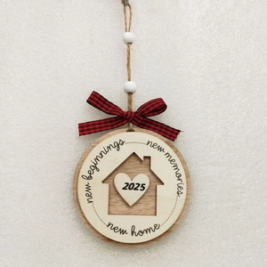 Detail of wooden 2025 new home ornament with engraved text and red plaid ribbon