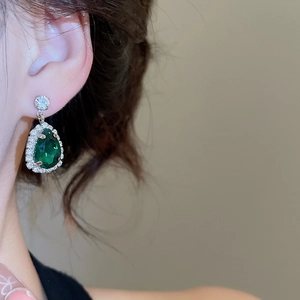 Macro detail of drop earrings featuring emerald green teardrop stones and silver setting