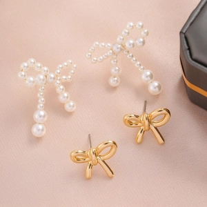 Detail of bow-shaped stud earrings set with white pearls and gold metal on pink satin