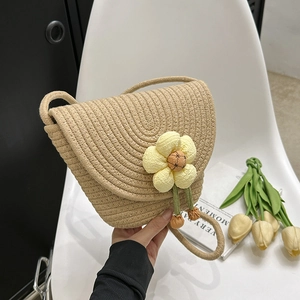 Detail of a woven beige straw crossbody bag with a 3D yellow flower and green tassel
