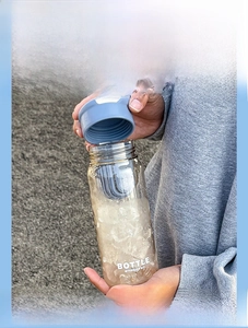 Detail of transparent water bottle with blue lid, tea filter and ice cubes in outdoor use