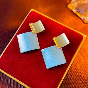 Macro shot of geometric square stud earrings in polished gold and brushed silver metal
