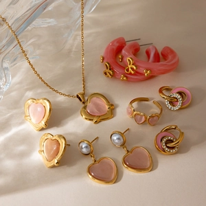 Macro detail of 18K gold-plated jewelry set with pink enamel hearts and pearls