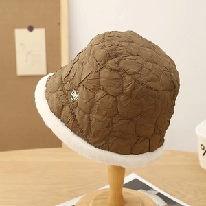 Close-up of brown quilted winter bucket hat with white faux fur trim and metal M logo