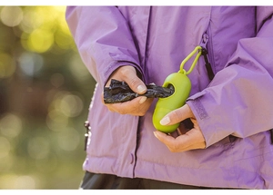 Green pill-shaped dog poop bag dispenser with LED light being used by a pet owner