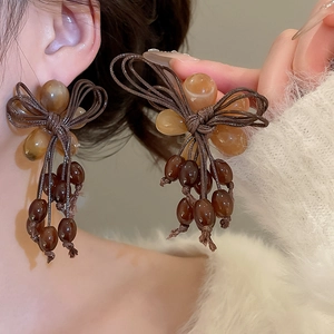 Macro detail of resin bow tassel earrings with brown beads on a female model