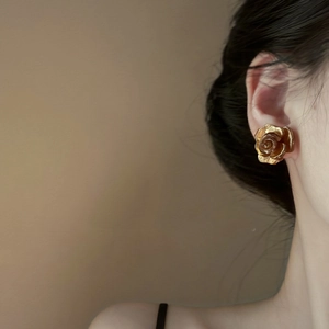 Close-up of model wearing gold rose-shaped layered earrings in a minimalist vintage style