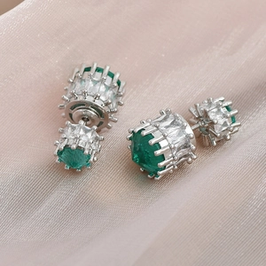 Close-up of emerald silver stud earrings with sparkling stones on pink silk fabric