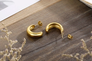 Close-up of golden C-shaped hoop earrings on dark wood with floral accents