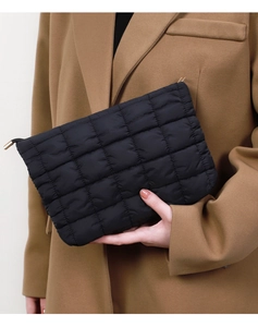 Detail of a black quilted clutch bag with metallic zipper held by a model