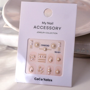 Detailed view of DIY nail art stickers with pearls and gold metal accessories in packaging