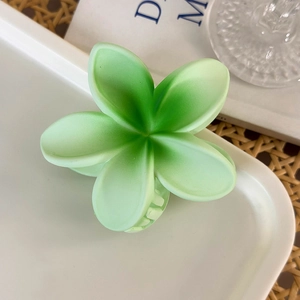 Macro shot of green gradient plumeria hair claw clip on a white tray with warm natural tones