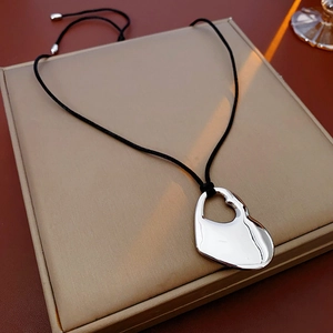 Close-up of a silver hollow heart-shaped pendant on a black cord over a gift box