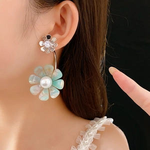 Detailed view of silver flower earrings with teal petals and a central pearl accent