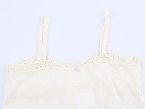 Détail de la dentelle en V et des broderies géométriques sur un caraco crème