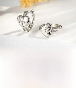 Detail view of silver heart earrings with lace cross pattern and pave diamonds