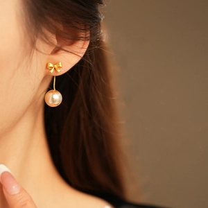 Close-up of a gold bow and pearl earring worn by a model in a French vintage style