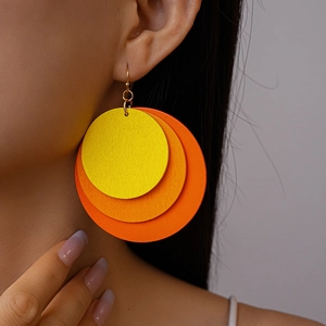 Close-up of a model wearing tiered round orange and yellow wooden earrings with gold hooks