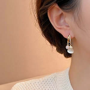 Close-up of gold earring with zircon inlay, white cat-eye stone, and pearl pendant on model