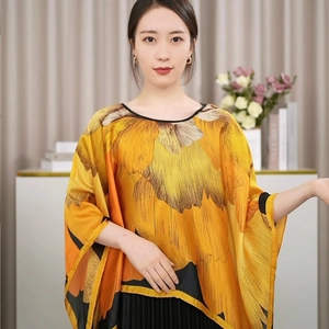 Detail eines goldenen Seidenponchos mit großen abstrakten Blumenmustern und schwarzen Säumen