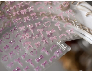 Macro detail of embossed pink bow and heart nail art stickers with pearl accents