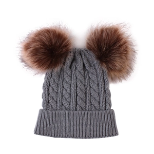 Close-up of grey cable knit baby hat with two large fluffy brown pom-poms on top