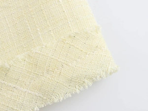 Gros plan du tissu en tweed jaune pâle avec fils dorés et détails de franges sur la robe