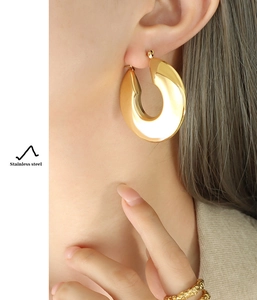 Detail of chunky gold U-shaped earrings and textured ring on model in stainless steel