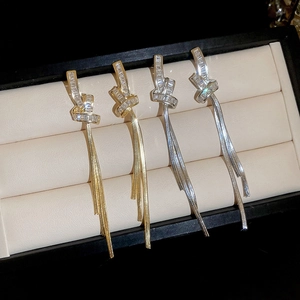 Detail of gold and silver knot earrings featuring zircon stones and long chain tassels