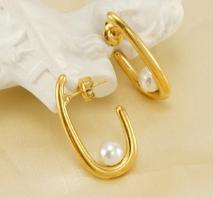 Detailed close-up of golden U-shaped earrings with white pearls on champagne fabric