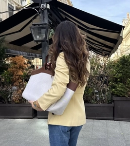 Close-up of a canvas tote bag with brown leather trim paired with a yellow blazer