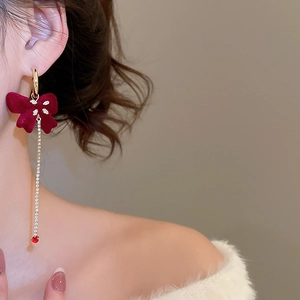 Close-up of red flocked bow earrings with rhinestone tassels worn by a female model