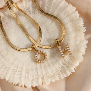 Close-up of 18K gold plated snake chain necklaces with pearl encrusted O and H letter charms