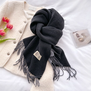 Close-up of black cashmere-like scarf with fringe and logo tag on beige coat