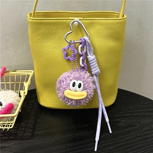 Close-up of purple plush monster keychain with yellow mouth on a textured bucket bag