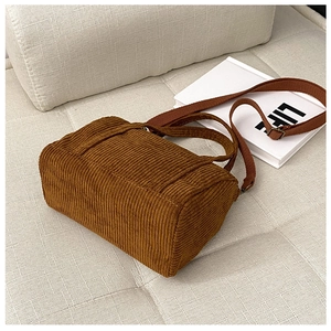 Detail of vintage brown corduroy Boston bag with handle and strap on a beige sofa