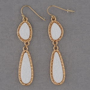 Detailed view of long teardrop gold earrings with white pear-shaped inlays and beaded edges