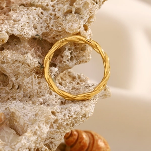 Macro detail of a twisted 18K gold-plated braided ring on a natural reef texture