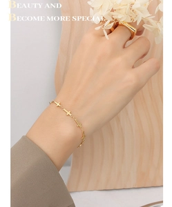 Detail of elegant gold cross chain bracelet on wrist against minimalist background