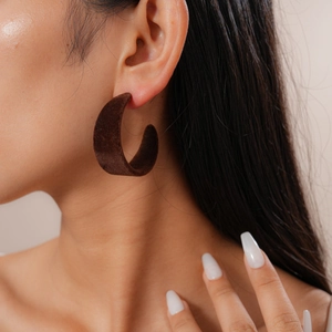Close-up of a retro deep brown flocked C-shaped earring worn on a model's ear lobe