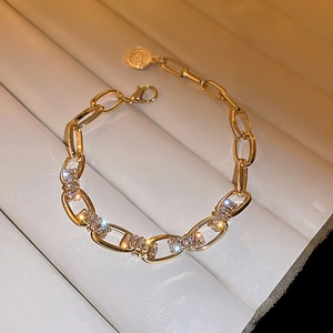 Detailansicht eines goldfarbenen Kettenglied-Armbands mit Zirkonia auf beige Kunstleder