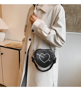 Dettaglio di una borsa a tracolla nera a forma di cuore con strass, catena argento e manico