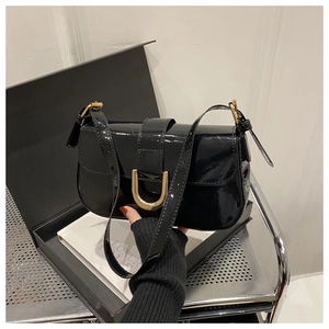Detail of glossy black patent leather handbag with a gold-tone horseshoe buckle and handle