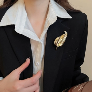 Golden leaf-shaped brooch with textured veins pinned on a black luxury suit jacket lapel