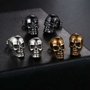 Gothic skull stud earrings in silver, gold, and black finishes on black leather stand