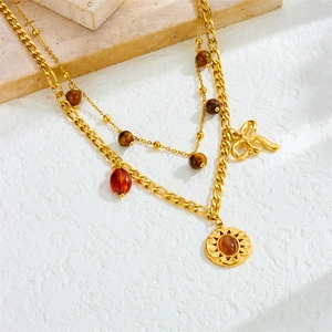 Layered gold necklace featuring a tiger eye stone sun pendant and bow charm detail