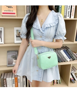 Detail of mint green woven crossbody camera bag with adjustable strap worn by a model