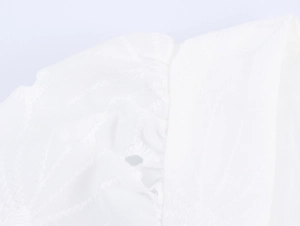 Vue macro des broderies florales blanches et du tissu en coton doux sur la robe