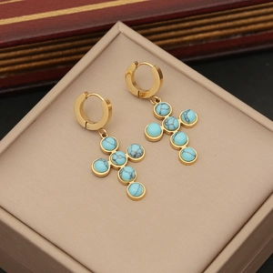 Detailed shot of golden cross earrings featuring inlaid turquoise beads on a jewelry box