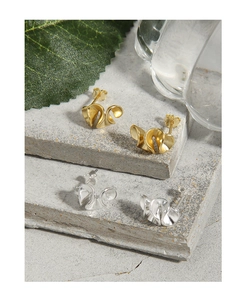Detailed view of silver and gold ruffle wave stud earrings on a stone surface